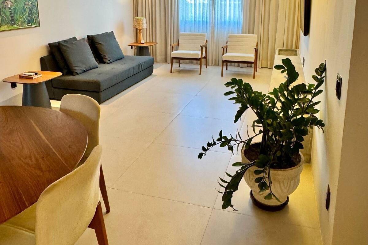 A modern living room with a sofa, two chairs, a dining table, and a potted plant.