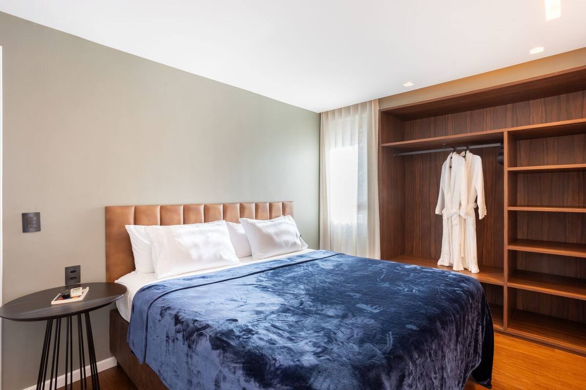 A modern hotel room with a large bed, a bedside table, a wardrobe, and a window with curtains.
