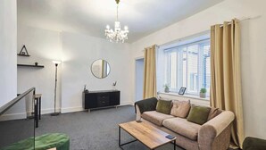 Ein modernes Wohnzimmer mit einer Couch, einem Couchtisch, einer Chandelüster, einem Spiegel und einem Fenster mit Vorhängen.