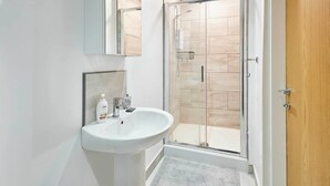 Une salle de bain moderne avec un lavabo blanc, une douche en verre et une porte en bois.