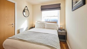 Une chambre bien rangée, avec un grand lit, une table de chevet avec une lampe, une fenêtre donnant sur un beau paysage et une porte.