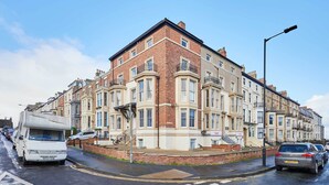 Une rangée de maisons mitoyennes avec une cour intérieure, un fourgon blanc garé dans la rue et un ciel bleu dégagé.