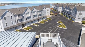 Une rangée de maisons de ville, avec un parking au premier plan et une étendue d’eau en arrière-plan.