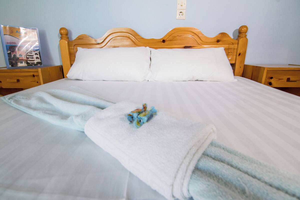 A neatly made bed with white linens and two pillows, a wooden headboard, and a folded towel on the bed.
