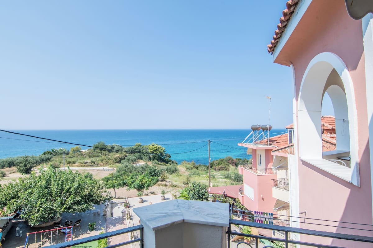 A pink building with a balcony overlooking a coastal area.
