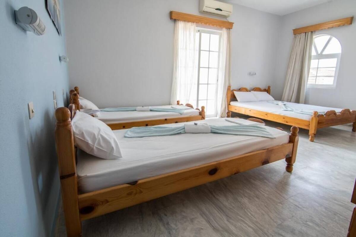 A room with three wooden beds, a window with curtains, and an air conditioning unit.