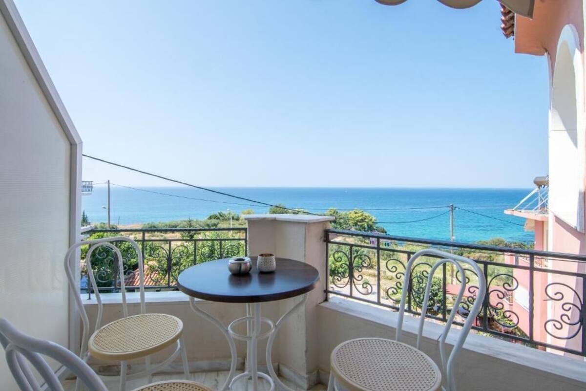 A balcony with a table and chairs, overlooking a coastal view.