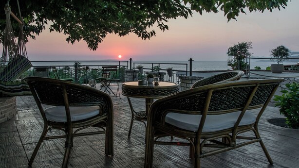 Un espace extérieur aménagé avec des chaises en osier et une table ronde, offrant une vue sur le coucher de soleil sur la mer.