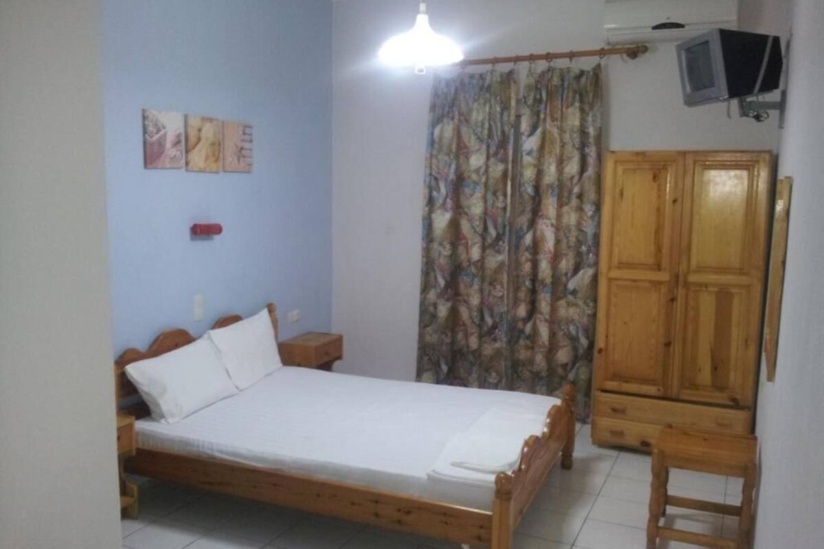 A bedroom with a wooden bed, a nightstand, a wardrobe, and a television mounted on the wall.