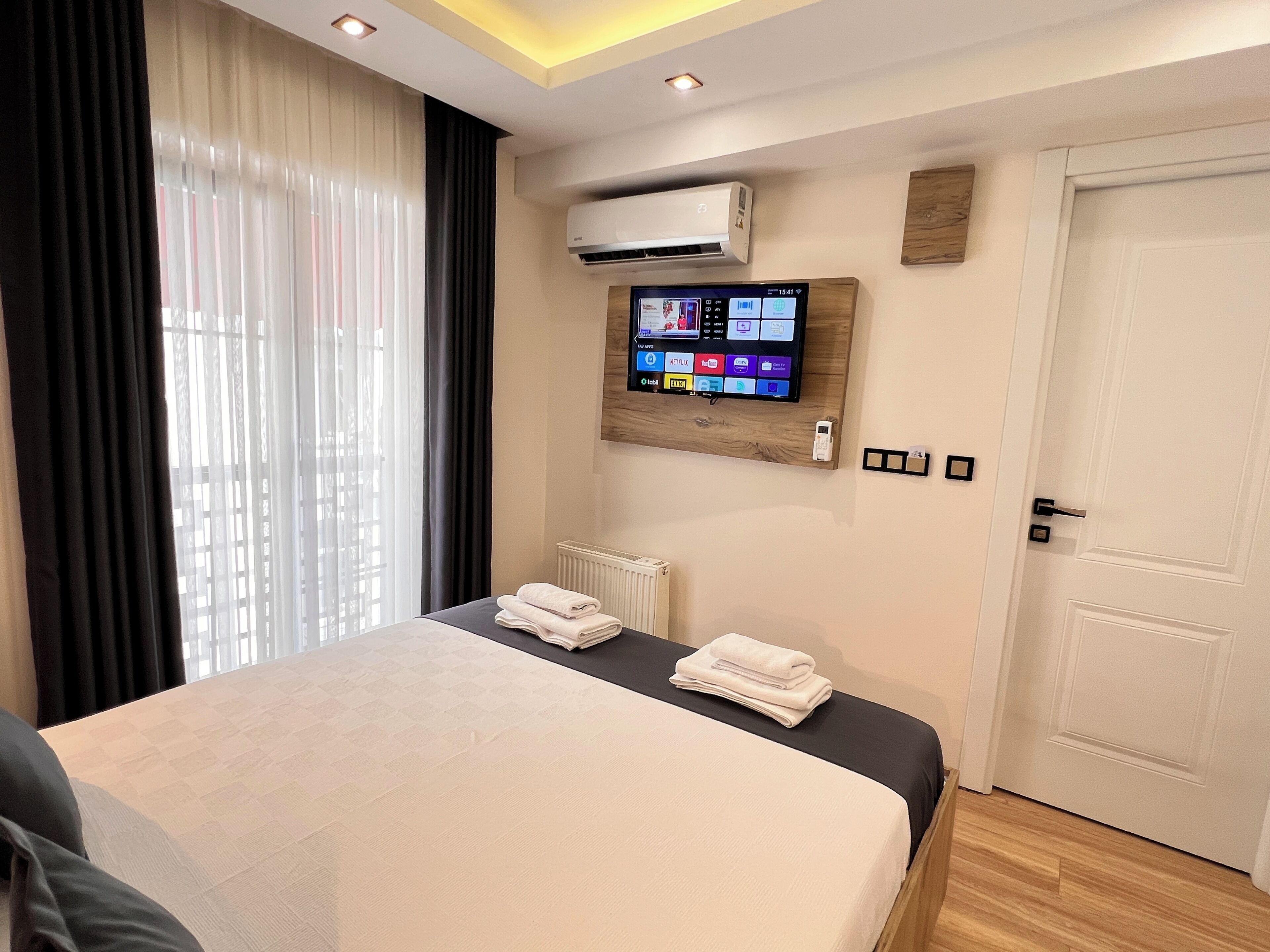 A modern hotel room with a large bed, a mounted TV displaying streaming services, and an air conditioning unit.