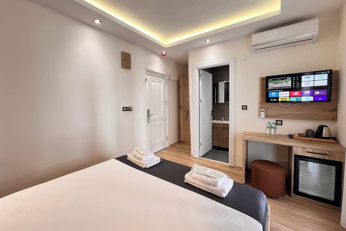 A hotel room with a bed, a desk with a TV, and a small kitchenette.