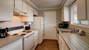 A compact kitchen with white cabinets, a stove, a refrigerator, and a microwave.