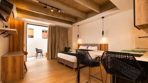 A modern hotel room with a bed, two black chairs, a desk, and a wooden floor. - Loft in Laureles with kitchenette, AC & workspace (Medellín)
