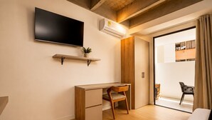 A modern room with a flat-screen TV, a desk with a chair, a small plant, and a sliding door leading to a balcony with outdoor seating. - Loft in Laureles with kitchenette, AC & workspace (Medellín)