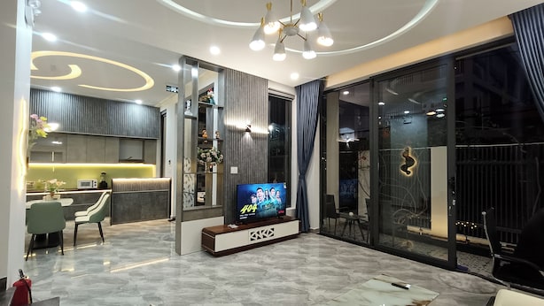 A modern living room with a flat-screen TV, a dining area, and a kitchen. - Aroma My Khe Beach (Da Nang)