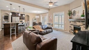A spacious living area with a fireplace, a kitchen with dark cabinetry, and a dining area with a table and chairs. - Spacious Retreat in West Omaha 2 King 3 Queen Beds (Omaha)