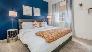 A bedroom with a bed, two bedside lamps, a blue accent wall, and a window with curtains. - Spacious Retreat in West Omaha 2 King 3 Queen Beds (Omaha)