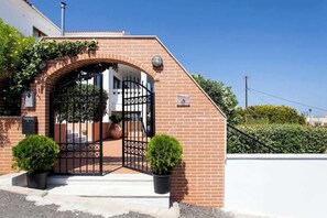 Un edificio in mattoni con un ingresso delimitato da un cancello, piante in vaso e un cielo azzurro intenso.
