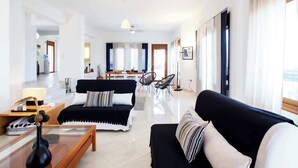 Een moderne woonkamer met een zwarte bank, een glazen salontafel en een eethoek op de achtergrond.