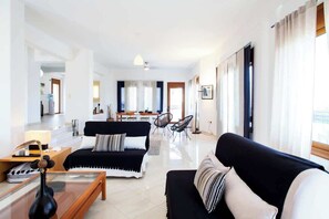 Una sala de estar moderna con un sofá negro, una mesa de centro de vidrio y un comedor al fondo.