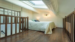 A bedroom with a skylight, wooden flooring, a bed with a white bedspread, and a wall-mounted light fixture. - Magnificient Duplex in Old Antibes ! (Antibes)