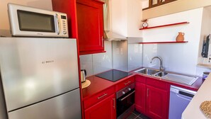 A compact kitchen with a Bosch refrigerator, red cabinets, a black induction cooktop, a stainless steel sink, and a dishwasher. - Magnificient Duplex in Old Antibes ! (Antibes)