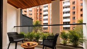A balcony with two black chairs, a round wooden table with snacks, and a view of a brick building with balconies. - Monthly Studio with kitchenette-AC-private balcony (Medellín)