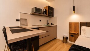 A compact kitchen with a microwave, coffee maker, and a small cabinet. There is a dining table with chairs and a bed with a wooden headboard. - Monthly Studio with kitchenette-AC-private balcony (Medellín)