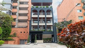A modern multi-story building with balconies, a central entrance, and surrounding greenery. - Monthly Studio with kitchenette-AC-private balcony (Medellín)