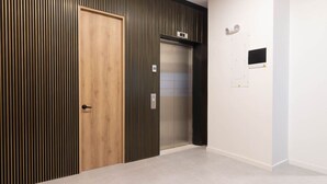 A hallway with a wooden door, a vertical striped wall, and an elevator.