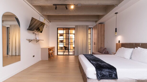 A modern hotel room with a large bed, a desk, and a view through a glass door.