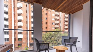 A balcony with two black chairs and a wooden table, overlooking a brick building with balconies.
