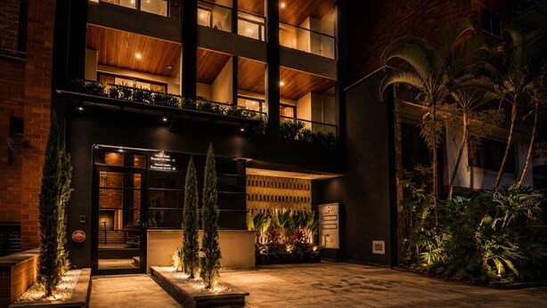 A hotel entrance with a dark facade, multiple balconies, and a well-lit entrance area with potted plants. - Loft in Laureles - AC fast WiFi & private balcony (Medellín)