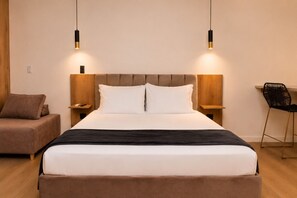A modern hotel room with a large bed, two bedside tables, a nightstand, a chair, and pendant lighting.
