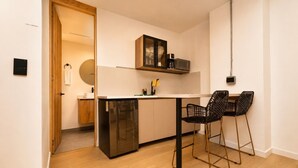A compact kitchen with a dishwasher, a coffee maker, and a small cabinet. There are two black chairs with a unique design.