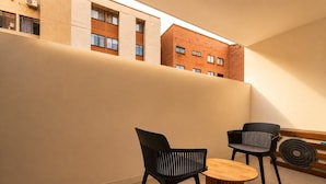 Un intérieur moderne avec une table ronde en bois et deux chaises noires, une grande fenêtre donnant sur un bâtiment en briques et un ventilateur fixé au mur.