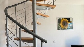 A modern spiral staircase with wooden steps and metal railings, a sofa, a television, and a sunflower painting on the wall. - Beautiful duplex with sea view AV-72 (ROSES)