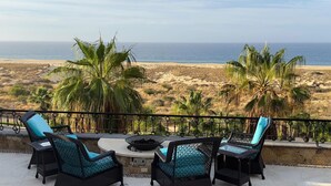 Eine Terrasse mit Korbmöbeln und Blick auf Strand und Meer.