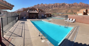 Une piscine sur le toit offrant une vue sur les montagnes, un espace salon couvert et une zone autour de la piscine délimitée par une clôture.
