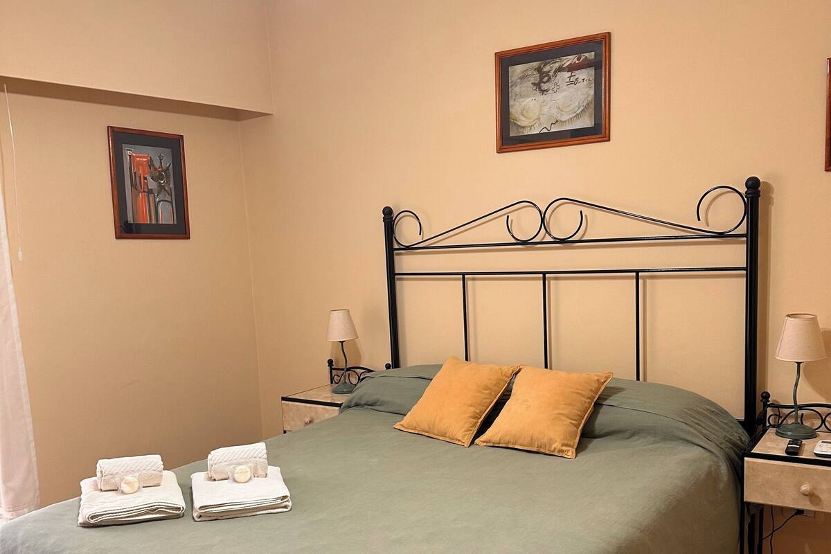 A neatly made bed with green bedding and two pillows, a ceiling fan, and a framed picture on the wall.