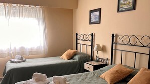 Une chambre d’hôtel avec deux lits, chacun agrémenté de draps verts et d’un oreiller marron. On y trouve une table de chevet avec une lampe et un tableau encadré au mur.