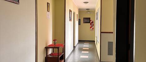 A hallway with a tiled floor, framed pictures on the walls, and a small table with a vase.