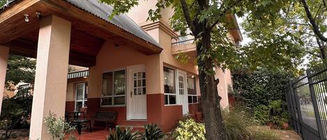 A house with a covered porch, a small garden, and a tree in front.