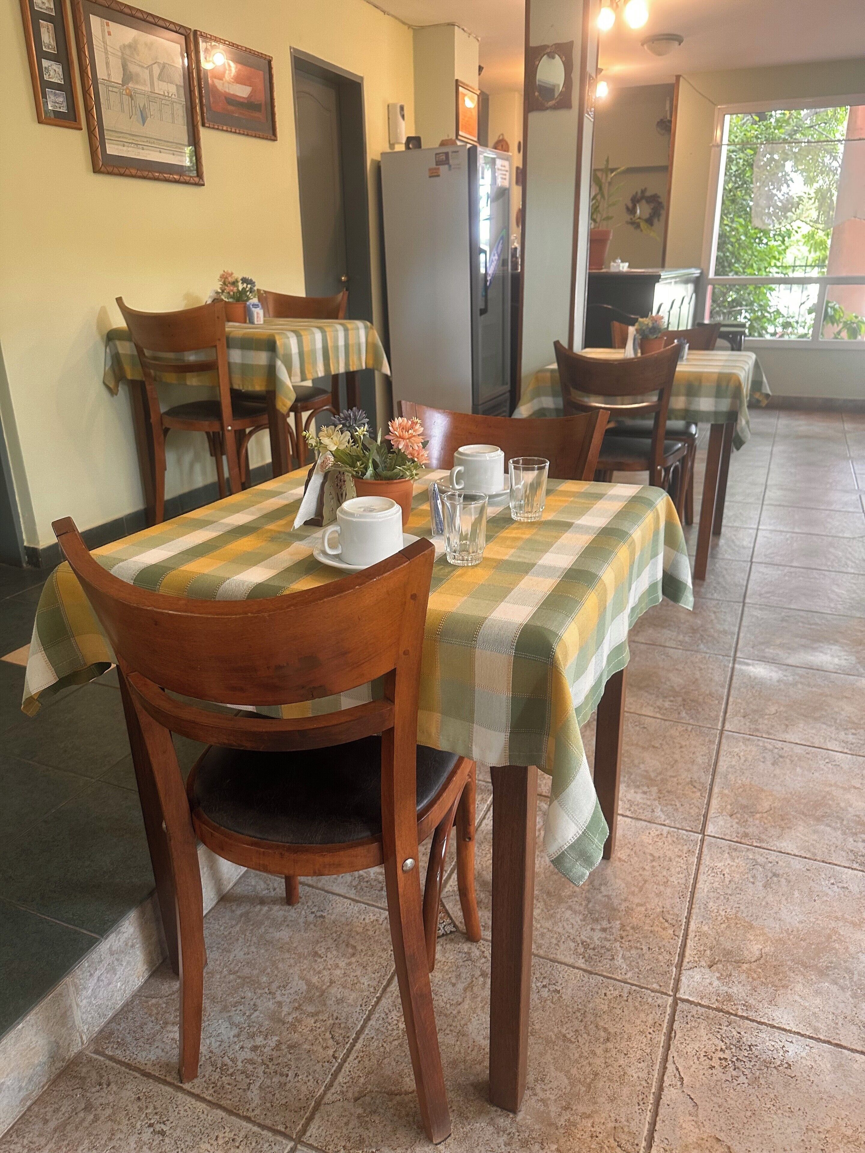 Un coin repas avec des nappes à carreaux, des chaises en bois et un réfrigérateur.