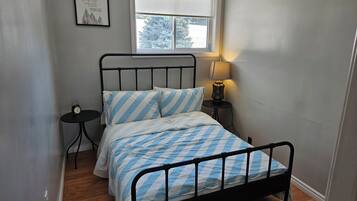 Une petite chambre à coucher, bien rangée, avec un lit, une table de chevet, une lampe et une citation encadrée accrochée au mur.