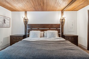 A bedroom with a wooden ceiling, a large bed with white bedding, two nightstands, and wall-mounted lamps.