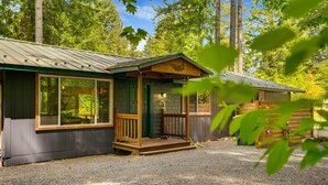 A cabin with a porch, large windows, and a gravel driveway.