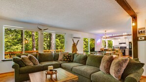 A cozy living room with a sectional sofa, a wooden coffee table, and a view of a lush green outdoor deck.