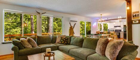 A cozy living room with a sectional sofa, a wooden coffee table, and a view of a lush green outdoor deck.