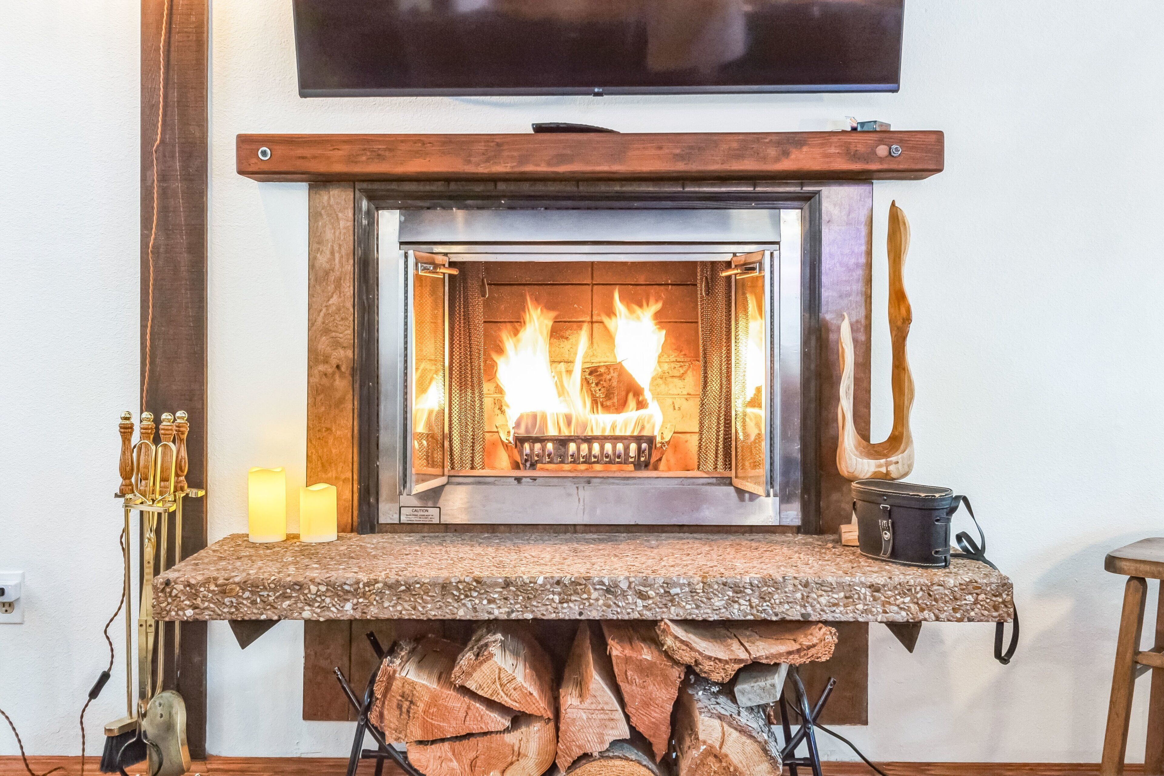 A fireplace with logs, a mantel, and a television above it.